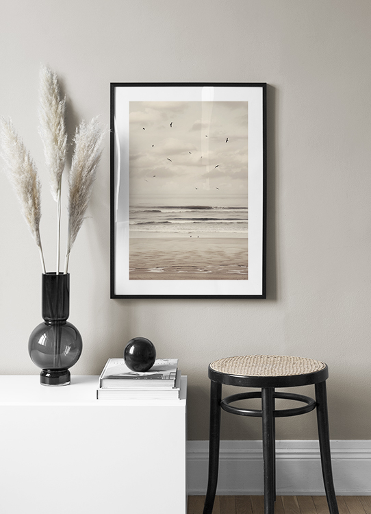  – Photograph of a beach and ocean with black birds flying in front of a cloudy sky