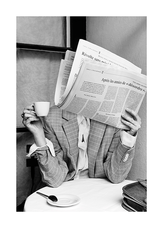  – Black and white photograph of a person sitting at a café table with a newspaper covering their face